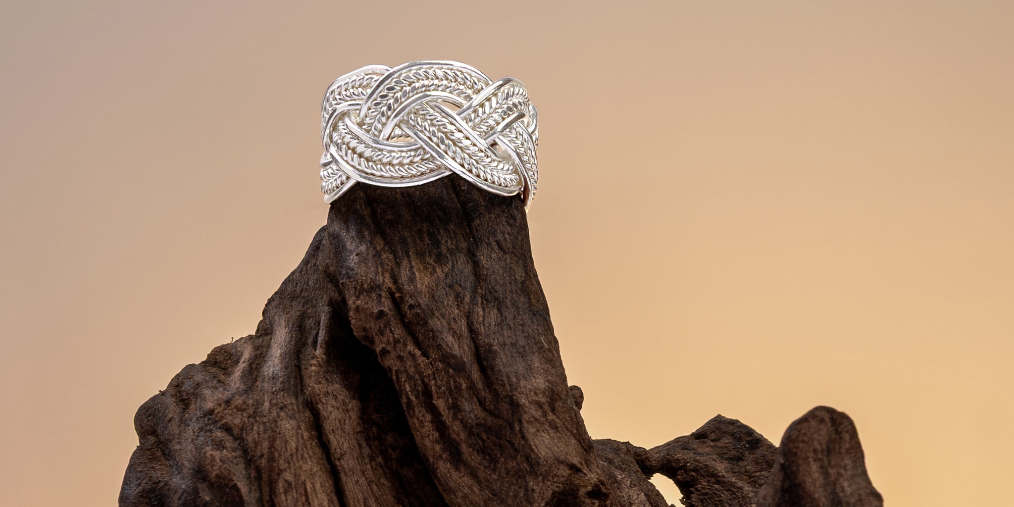 Bague tressée en argent massif posée sur une racine de bois, fond ocre – Itsara