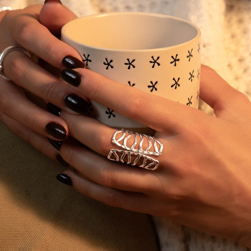 Modèle féminin tenant une tasse avec sur sa main une grande bague en argent massif contemporaine N°68 faite à la main - Itsara bijoux