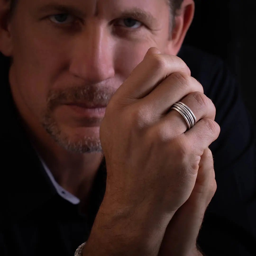 Modèle masculin, portant une bague artisanale en argent massif présente un fil torsadé et des finitions patinées pour un look à la fois rustique et sophistiqué.