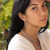 Modèle féminin portant un haut blanc avec des boucles d'oreilles en argent massif ethnique N°24 sur un fond de feuilles fabriqué entièrement à la main ainsi que 2 colliers chaines en argent massif sur fond de verdure - Itsara bijoux