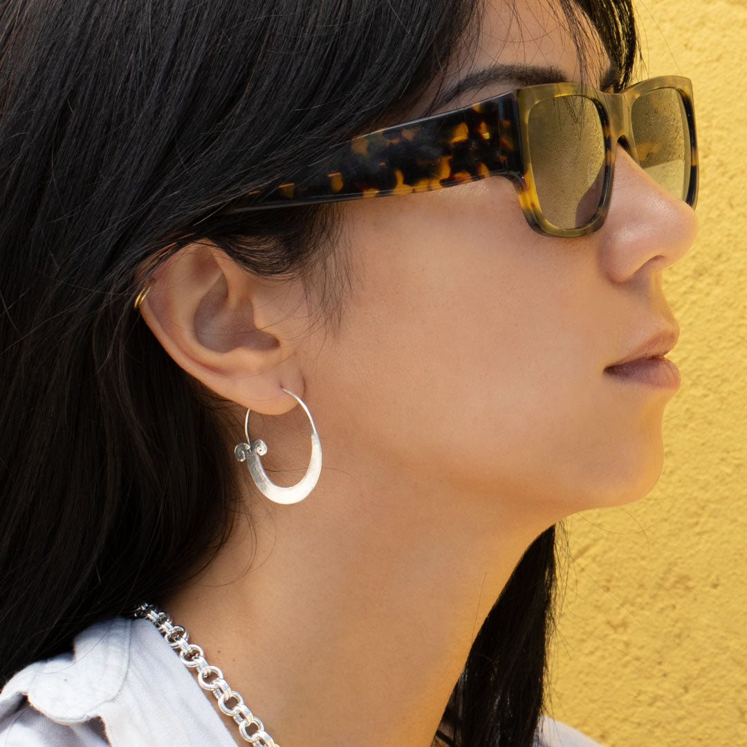 Boucles d'oreilles artisanales ethniques créoles en argent massif, spirales N°01 boucles traditionnelles des tribus d'Asie du Sud-Est portées par une femme avec le collier N°20 sur fond jaune ensoleillé. Une photo rapprochée - Itsara Bijoux