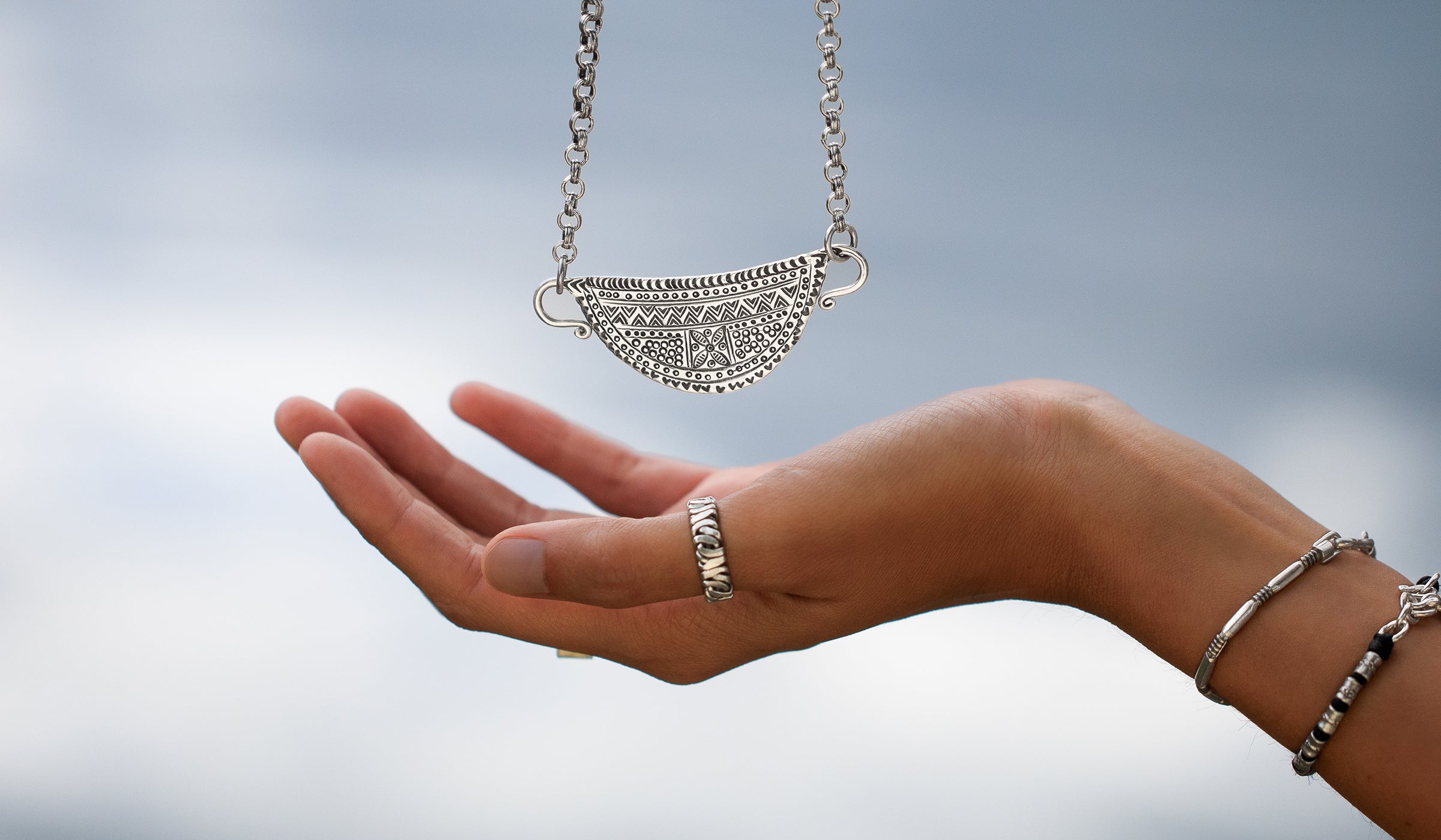 Collier à pendentif demi-lune en argent massif poinçonné de motifs ethniques, au-dessus d'une main – Itsara