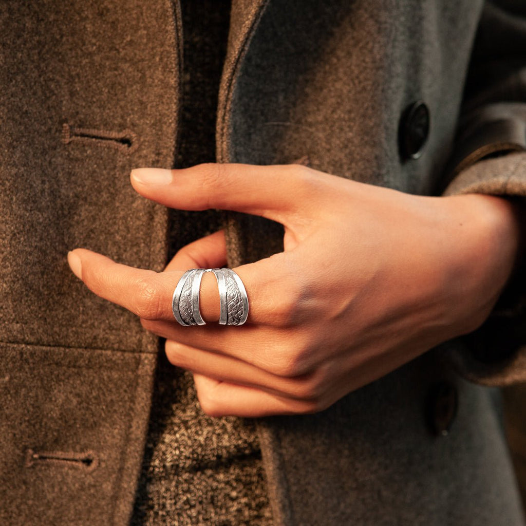 Grande bague artisanale en argent massif, entièrement faite à la main. Son design poinçonné et patiné crée une texture originale, tandis que le ruban d'argent ajoute une touche contemporaine et audacieuse.