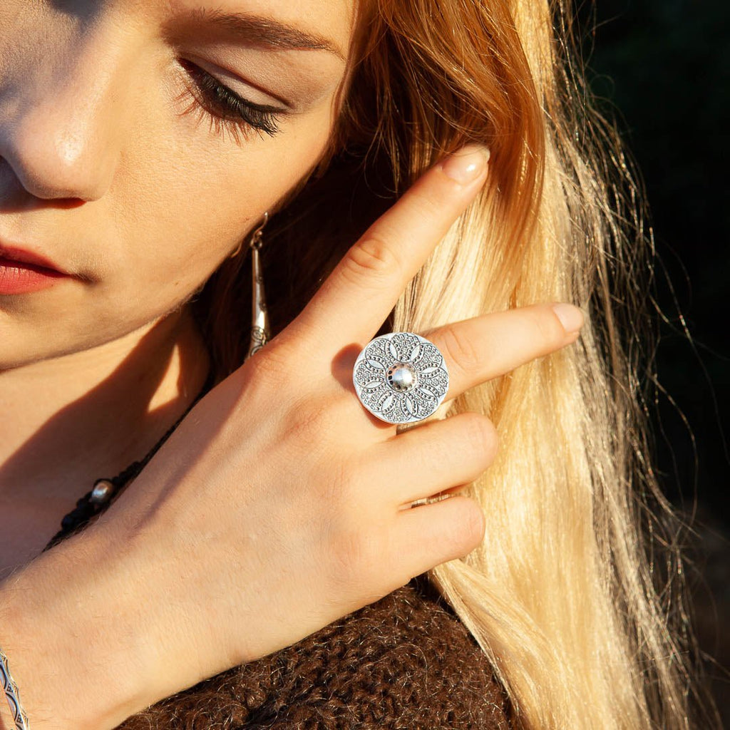 Femme portant une bague artisanale en argent massif avec un plateau orné de motifs floraux, bijou ethnique fait main.