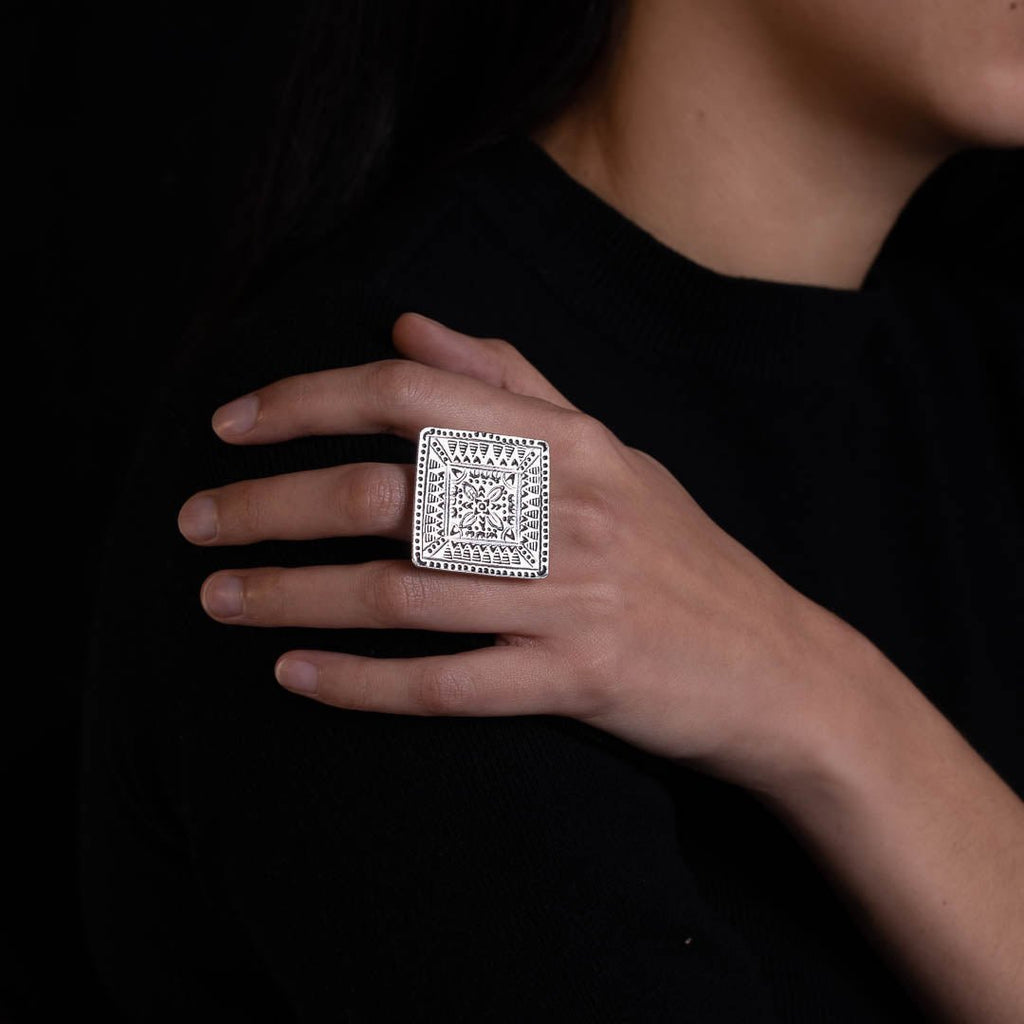 Femme portant une bague artisanale en argent massif avec un plateau carré orné de motifs géométriques, bijou symbolisant la nature et la stabilité