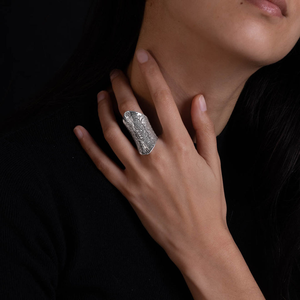 Bague en argent massif ethnique N°82 portée par une femme, design ethnique travaillé en repoussé avec des détails tribaux et floraux. Ce modèle de bouclier long est à la fois élégant et puissant, mettant en valeur les motifs poinçonnés à main levée. La patine accentue le contraste pour une allure intemporelle - Itsara bijoux