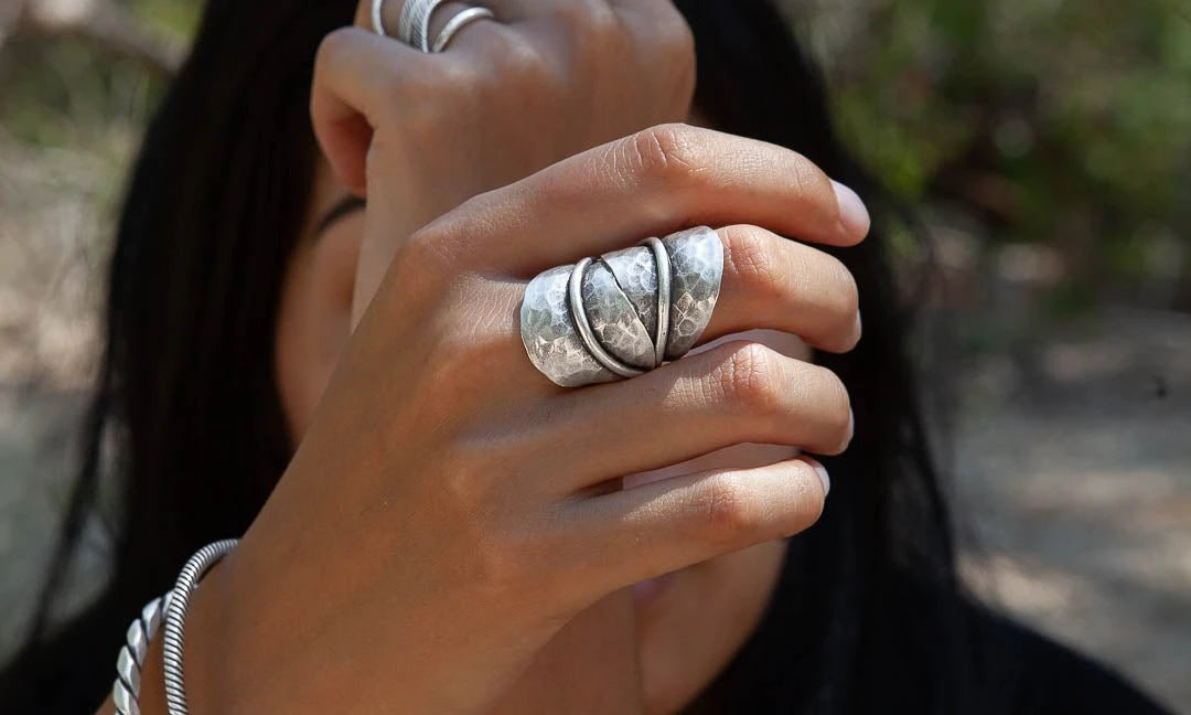 La grande bague en argent N°10 pour femme Itsara Bijoux est une pièce originale et remarquable. Ses deux belles feuilles martelées s’enlacent élégamment autour de votre doigt, ajoutant une touche audacieuse à toute tenue. Bague portée par un modele féminin avec en fond la nature - Itsara bijoux