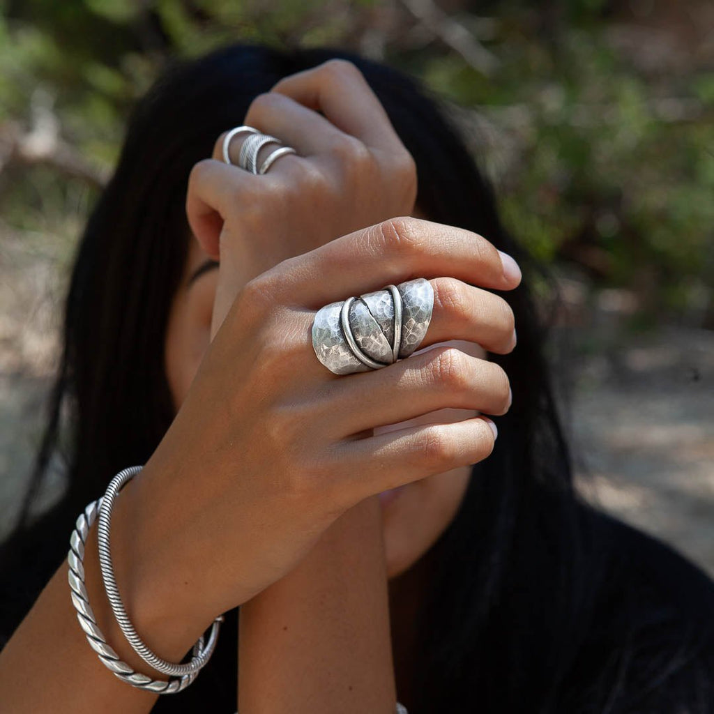 La grande bague en argent N°10 pour femme Itsara Bijoux est une pièce originale et remarquable. Ses deux belles feuilles martelées s’enlacent élégamment autour de votre doigt, ajoutant une touche audacieuse à toute tenue. Bague portée par un modele féminin avec en fond la nature - Itsara bijoux